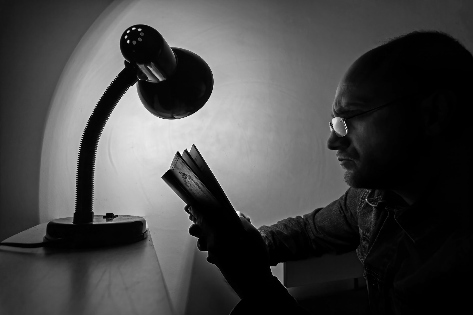 A man reading by the light of a desk lamp in a dark room